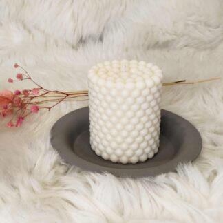Bougie artisanale Perle en cire d'olive sur un support gris, avec un bouquet de fleurs séchées, fond blanc cassé.