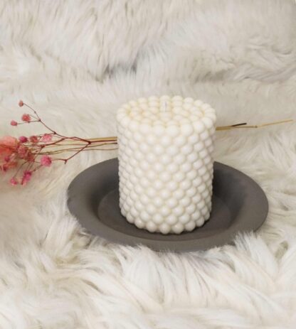Bougie artisanale Perle en cire d'olive sur un support gris, avec un bouquet de fleurs séchées, fond blanc cassé.